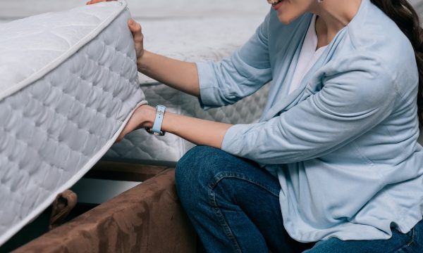 cropped shot of smiling woman choosing orthopedic mattress in furniture store